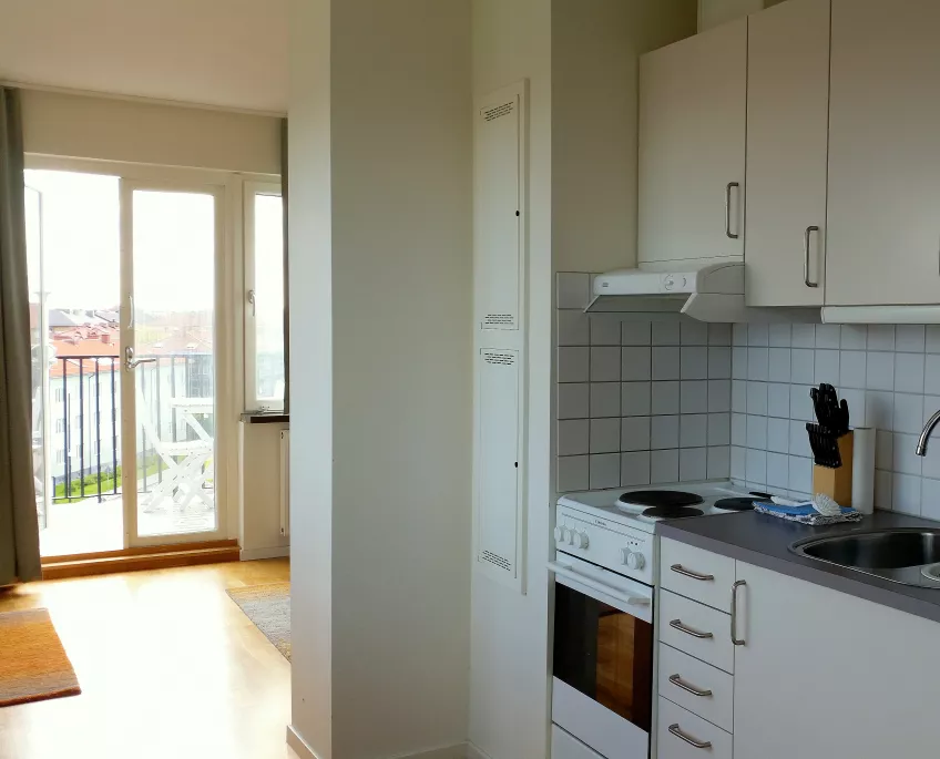 Overview over kitchen in an apartment at the housing area Folkets park showing the cooking area with cooker, sink and cupboards to the right and the balcony to the left (picture)