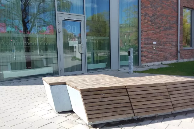 LU Accommodation Sofieberg reception entrance; a wood-covered concrete bench in front of a door in a glass wall. Photo by Mikko Jokela Måsbäck.