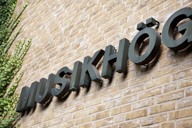 A grey sign on a brick wall spelling out Musikhög(skolan), i.e. "Malmö Academy of Music". Photo by Charlotte Carlberg Bärg