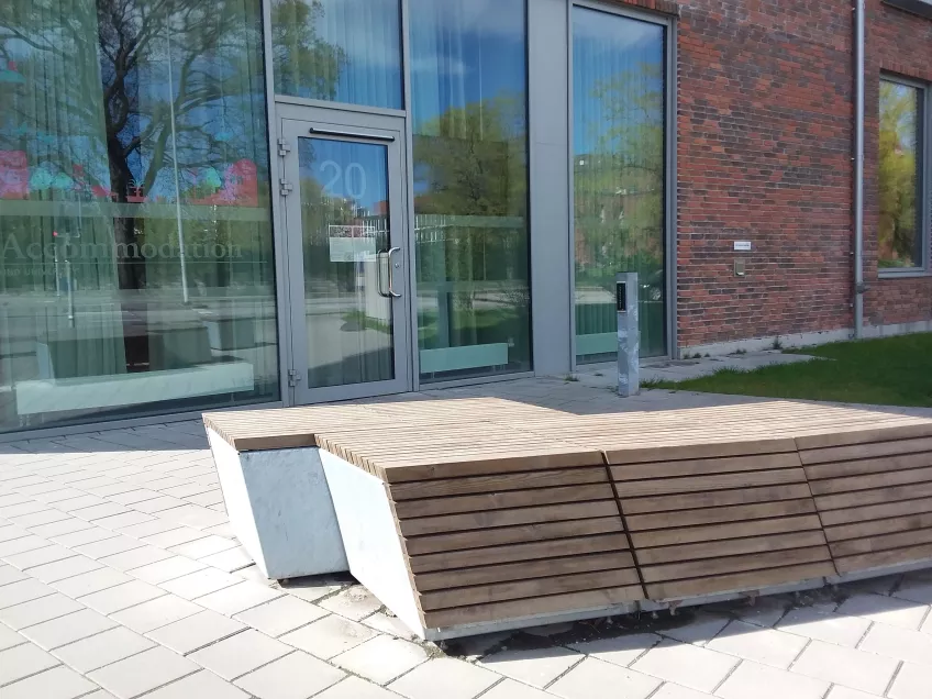 LU Accommodation Sofieberg reception entrance; a wood-covered concrete bench in front of a door in a glass wall. Photo by Mikko Jokela Måsbäck.