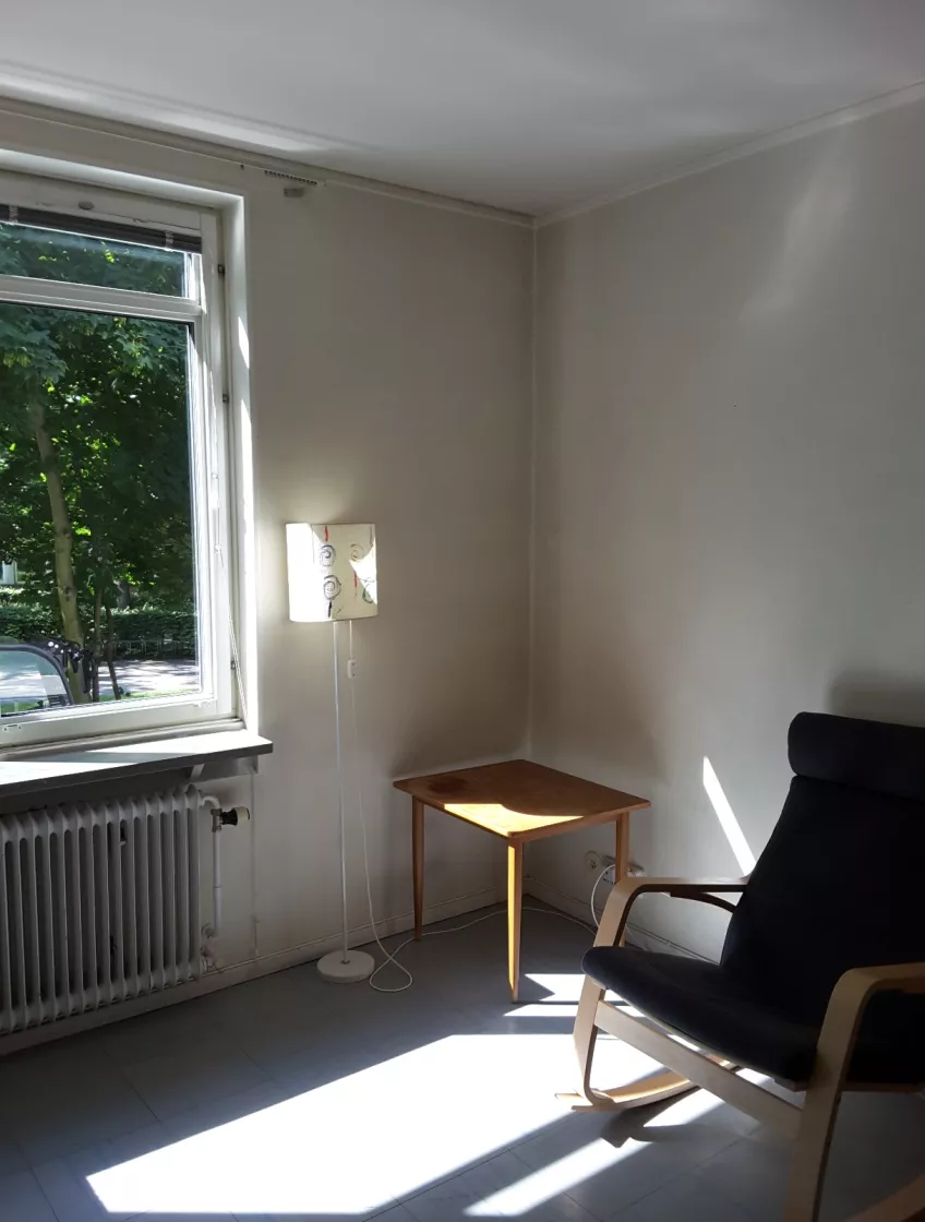 Overview of room E1109 at housing area Michael Hansen showing the window, floor lamp, side table and armchair.