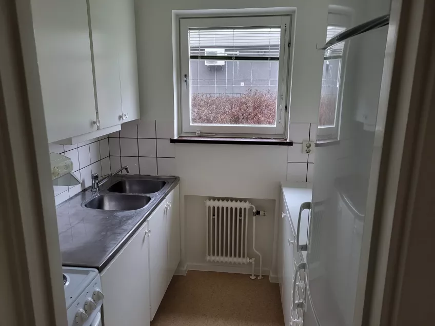 View of a small kitchen with a central window, sink and oven to the left, and fridge/freezer to the right. Photo: Mikko Jokela Måsbäck