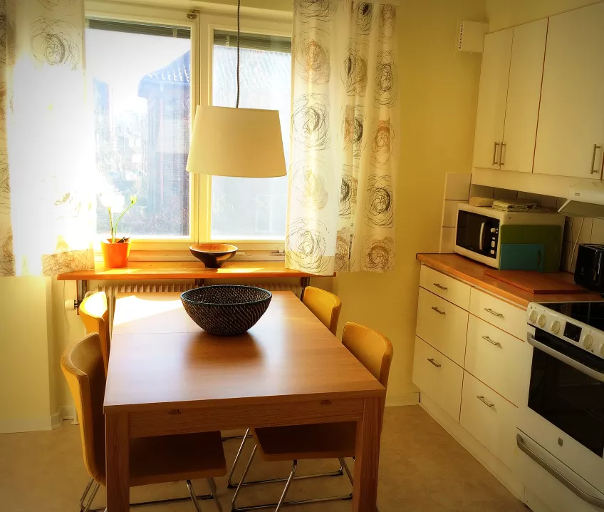 A photo of a kitchen at Gerdagatan 13 showing a table, a window, and a counter with a stove and cabinets (photo).