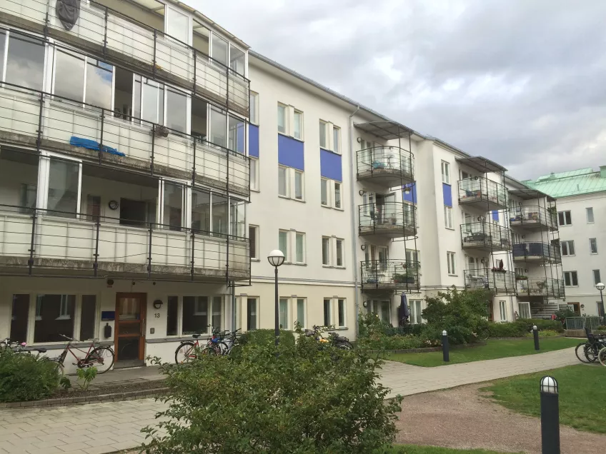 Side on view of a four story white building with blue detailing, and a courtyard with gravel path and bushes in front. Photo by LU Accommodation.